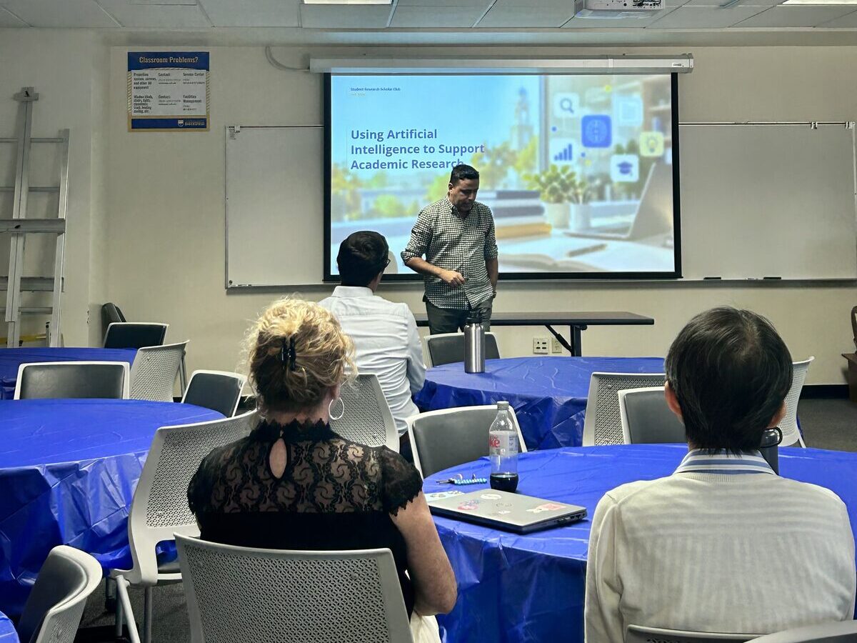 Dr. Milad Pira presenting "Using Artificial Intelligence to Support Academic Research" to students seated at round tables